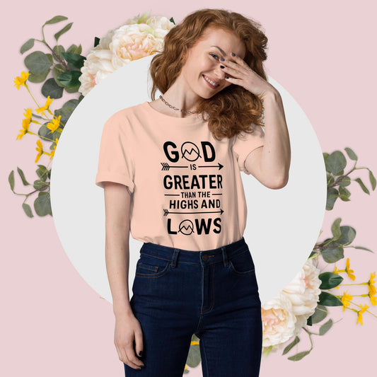 A woman smiles, covering her face, wearing a peach "God is Greater Than the Highs and Lows" t-shirt.